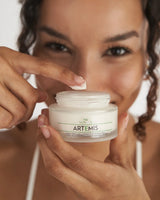 Woman holding jar and applying VOVEES Artemis anti-wrinkle cream for deep hydration and youthful skin.