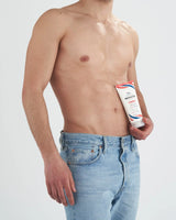 Shirtless man holding a tube of VOVEES LipoCream Corpo Termogenica body cream in blue jeans against white background