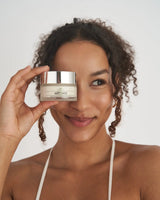 Donna sorridente che mostra la crema viso antirughe VOVEES Artemis per pelle idratata e giovane.